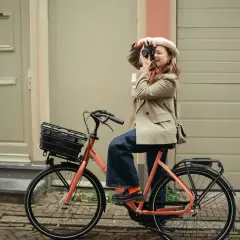 Vrouw met camera op een oranje fiets, klaar voor de beste elektrische fiets 2026.