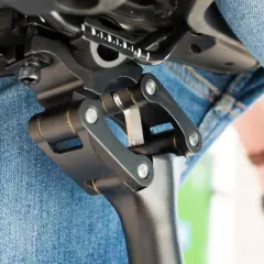 Gedetailleerde close-up van een fietszadel met een verende zadelpen afstellen. De mechanische delen zijn duidelijk zichtbaar, met een persoon in spijkerbroek op de achtergrond.