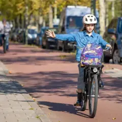 Meisje op fiets met rugzak en helm geeft richting aan, een voorbeeld van verkeersregels voor fietsers.