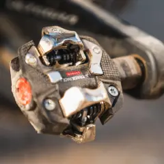 Close-up van een vuil racefiets pedaal met een carbon X-Track Race kliksysteem, klaar voor de volgende rit.