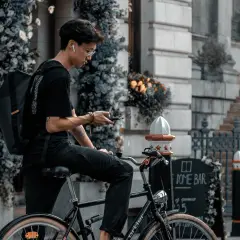 Jonge man op fiets met rugzak, kijkend op zijn telefoon. Is een fietser altijd beschermd in het verkeer?