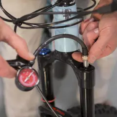 Iemand stelt de verende voorvork van een e-bike af met een pomp en manometer.