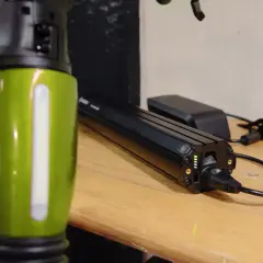 Een groene e-bike frame staat naast een Bosch accu die aan het opladen is. De accu heeft groene lampjes die de laadstatus aangeven.
