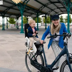 Een hippe mamafiets met een lachend kindje in de kinderzitje, klaar voor een ritje onder een stationskap.