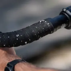 Een hand die het nieuwe, zwart-witte stuurlint vervangt op een racefietsstuur.