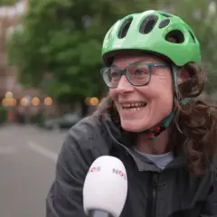 Vrolijke vrouw met groene fietshelm en bril, lachend in de camera. Ze vertelt over de fietshelm verplicht in Duitsland.