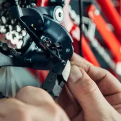 Hand knipt versnellingskabel fiets. De derailleur en ketting zijn zichtbaar, met een rode fietsframe op de achtergrond.