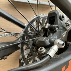 Close-up van een fietsremklauw, klaar voor het bijvullen van hydraulische remmen. De schijfrem en ketting zijn zichtbaar.