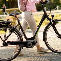 Vrouw loopt met elektrische fiets, de kilometerstand is niet zichtbaar, maar de fiets is klaar voor een rit.