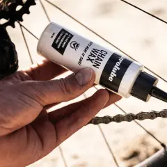Hand brengt kettingwax aan op de fietsketting voor soepel fietsen.
