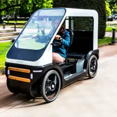 Een vrouw rijdt in een moderne fiets met dak door een park. De fiets heeft een strak design en biedt bescherming tegen het weer.