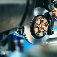 Monteur werkt aan schijfremmen schoonmaken. De remklauw wordt met een schroevendraaier losgemaakt.