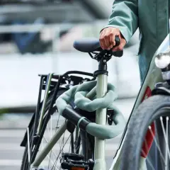 Een persoon met een groene jas houdt het zadel van een fiets vast. De fiets is beveiligd met een lichtgroene kettingslot. Denk aan een gps tracker fiets inbouwen voor extra veiligheid.
