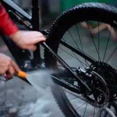 Iemand maakt de fietsketting schoon met Dasty, terwijl de rest van de fiets nat wordt gespoten.
