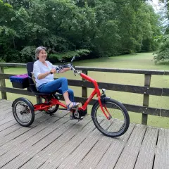 Vrolijke vrouw geniet op een driewieler, een veilige fiets voor ouderen, langs een groen kanaal.