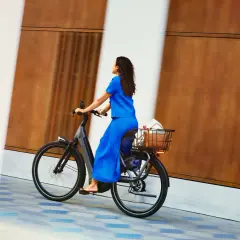 Vrouw in blauwe jurk geniet van een ritje op haar nieuwe fiets, met boodschappen in de mand. Een perfecte fiets kiezen is een feest!
