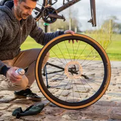 Man onderhoudt fietswiel met remschijf. Hij spuit met een busje, mogelijk voor het handrem fiets afstellen.