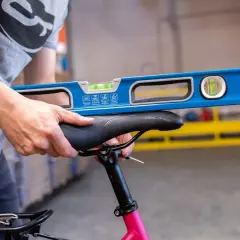 Een persoon gebruikt een waterpas om het fietszadel af te stellen. De waterpas ligt op het zadel om te controleren of het recht staat.