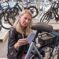 Vrouw overweegt wel of geen elektrische fiets in een fietsenwinkel, omringd door diverse modellen.