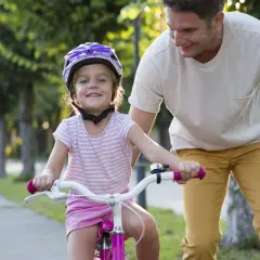 Een vader leert zijn dochter fietsen, met een helm op voor haar veiligheid. Zo zorgen we ervoor dat elk kind veilig op de fiets zit.