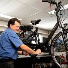 Man werkt aan een fiets, mogelijk om deze om te bouwen naar een driewieler.