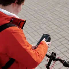 Bezorgbezorger in oranje jas checkt zijn telefoon op de fiets, hopelijk geen boete telefoon fiets!