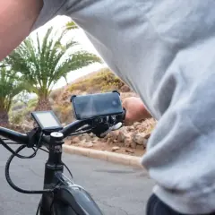 Persoon op een speed pedelec, die een motorvoertuig is, met telefoonhouder en display. Palmbomen op de achtergrond.