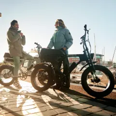 Twee mensen bij hun fatbikes aan het water. De vraag "hoe zwaar is een fatbike" komt op, maar deze stoere e-bikes lijken verrassend licht.