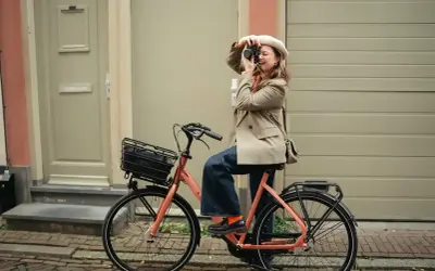Vrouw met camera op een oranje fiets, klaar voor de beste elektrische fiets 2026.