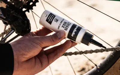 Hand brengt kettingwax aan op de fietsketting voor soepel fietsen.