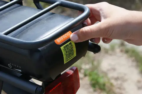 Hand plaatst sticker met QR-code op e-bike accu. Dit is een gestolen fiets register om diefstal te voorkomen.