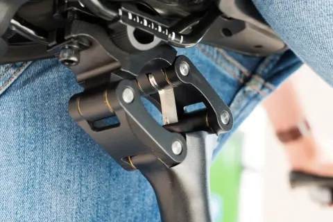 Gedetailleerde close-up van een fietszadel met een verende zadelpen afstellen. De mechanische delen zijn duidelijk zichtbaar, met een persoon in spijkerbroek op de achtergrond.