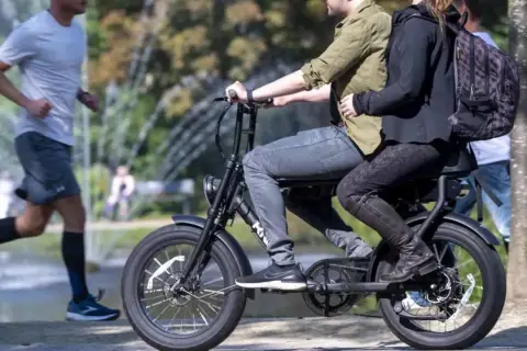 Een stel rijdt op een fatbike, terwijl een hardloper ernaast rent. Nadelen fatbike: minder beweging, meer overlast.