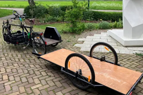 Een fiets met een bakfiets-achtige constructie en een aanhanger, klaar om een zijspan fiets te maken.
