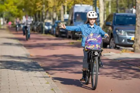 Meisje op fiets met rugzak en helm geeft richting aan, een voorbeeld van verkeersregels voor fietsers.