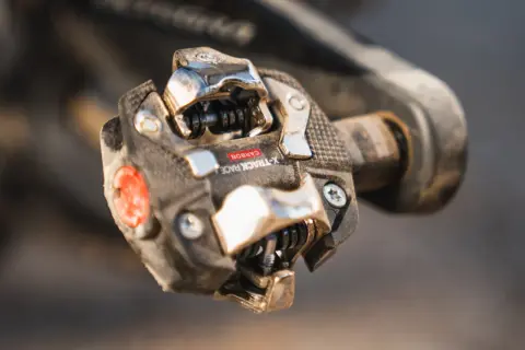 Close-up van een vuil racefiets pedaal met een carbon X-Track Race kliksysteem, klaar voor de volgende rit.