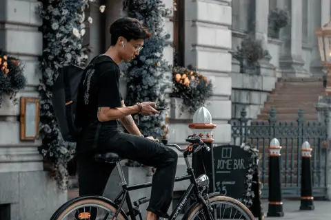 Jonge man op fiets met rugzak, kijkend op zijn telefoon. Is een fietser altijd beschermd in het verkeer?