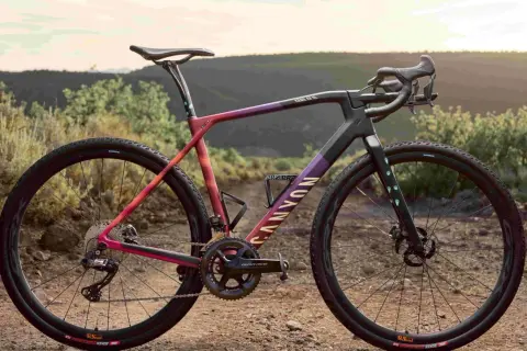 Een kleurrijke Canyon fiets, ideaal voor cyclocross vs gravel bike avonturen, staat in een droog, heuvelachtig landschap.