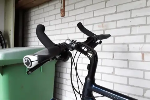 Stuur van een fiets met handvatten en een bel. Geen mountainbike bar ends te zien, wel een groene bak ernaast.