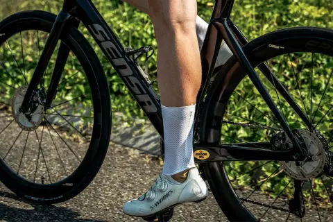 Een wielrenner met witte sokken en schoenen, op een racefiets met hoge velgen. De fiets is zwart met een Sensa frame.