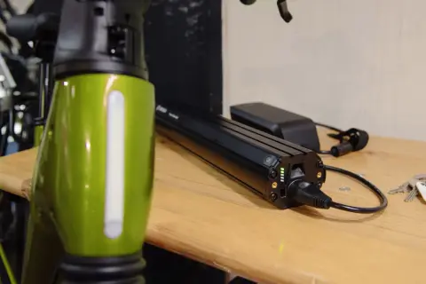 Een groene e-bike frame staat naast een Bosch accu die aan het opladen is. De accu heeft groene lampjes die de laadstatus aangeven.