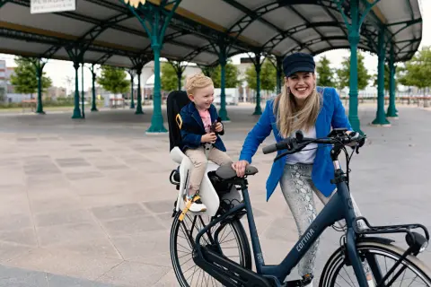 Een hippe mamafiets met een lachend kindje in de kinderzitje, klaar voor een ritje onder een stationskap.