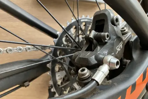 Close-up van een fietsremklauw, klaar voor het bijvullen van hydraulische remmen. De schijfrem en ketting zijn zichtbaar.