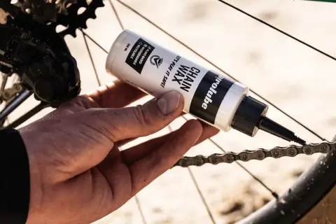 Hand brengt kettingwax aan op de fietsketting voor soepel fietsen.