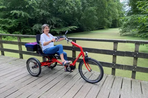 Vrolijke vrouw geniet op een driewieler, een veilige fiets voor ouderen, langs een groen kanaal.