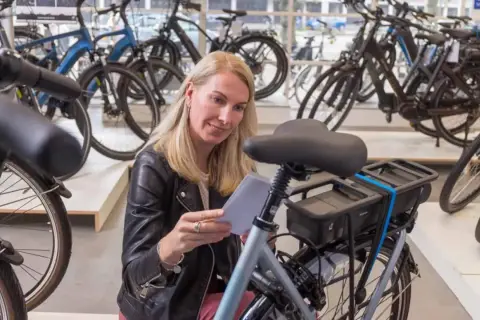 Vrouw overweegt wel of geen elektrische fiets in een fietsenwinkel, omringd door diverse modellen.