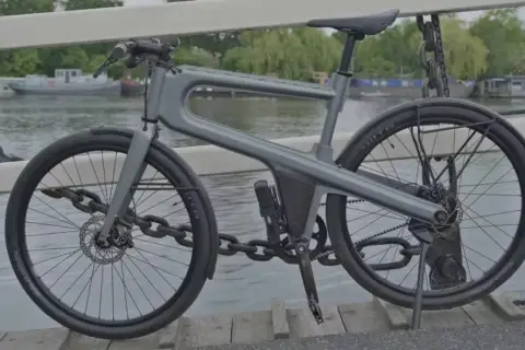 Moderne, hippe stadsfiets met een uniek frame, geparkeerd op een brug met uitzicht op boten.