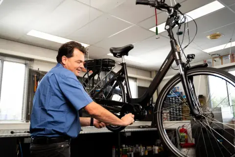 Man werkt aan een fiets, mogelijk om deze om te bouwen naar een driewieler.