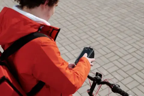 Bezorgbezorger in oranje jas checkt zijn telefoon op de fiets, hopelijk geen boete telefoon fiets!