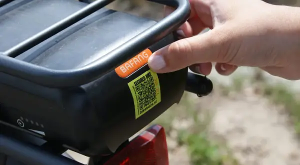 Hand plaatst sticker met QR-code op e-bike accu. Dit is een gestolen fiets register om diefstal te voorkomen.